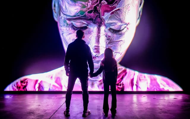 Adult and child silhouetted before a giant glowing immersive digital art face in Amsterdam