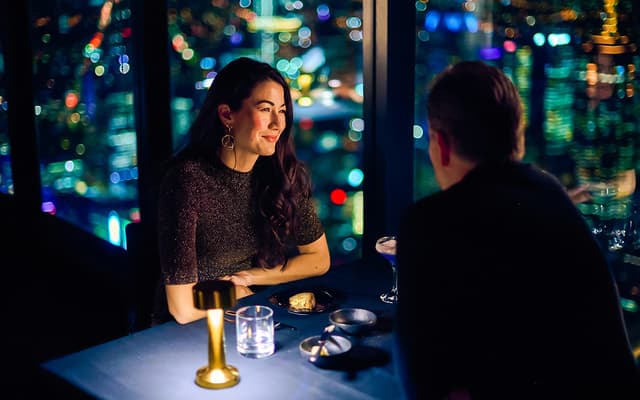 Couple dining at a high-rise restaurant in Melbourne with city skyline lights through tall windows