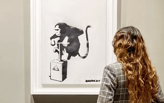 Visitor viewing a framed Banksy monkey print at the Moco Museum in Barcelona