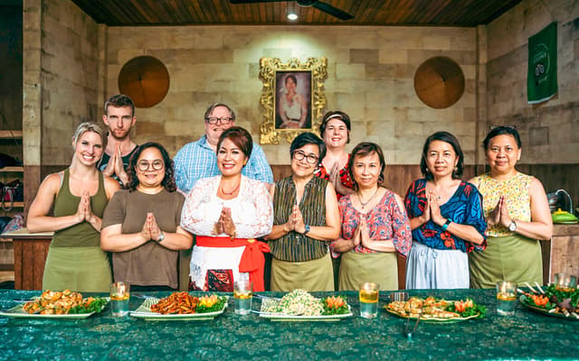 Group at a Balinese cooking class in Ubud doing the namaste gesture behind plated local dishes
