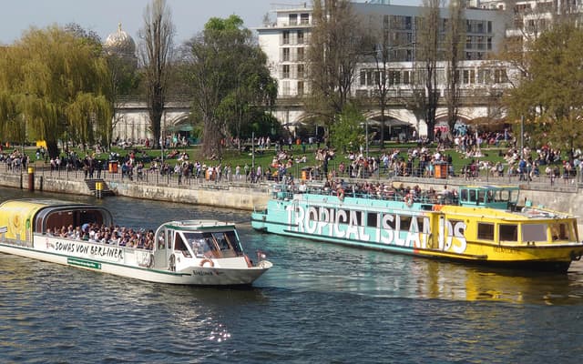 Sightseeing cruise boats on the River Spree passing crowded riverbanks in central Berlin