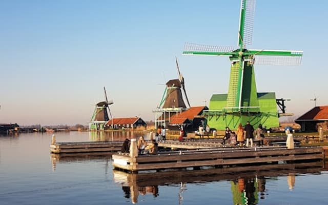 Green and traditional Dutch windmills reflected in calm water at Zaanse Schans near Amsterdam