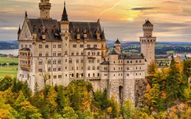 Neuschwanstein Castle on a forested hilltop at sunset above the Bavarian countryside