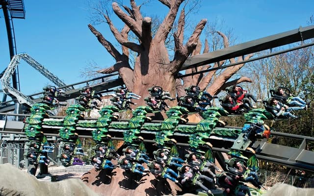 Riders on a spinning green theme-park ride around a tree centrepiece at a park near Verona