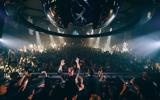 DJ raising his arms to a packed crowd under stage lights in an Ibiza nightclub at night