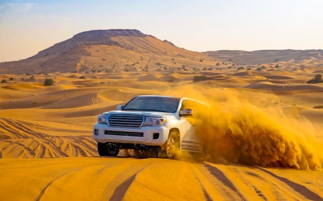 White 4x4 speeding through golden desert dunes on an Abu Dhabi safari