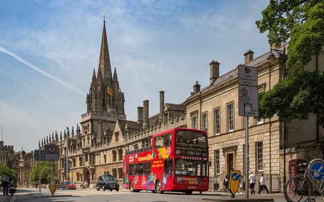 Red open-top sightseeing bus on Oxford High Street below the spire of St Mary the Virgin