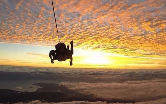 Tandem skydivers under a parachute descending through a glowing sunset sky above Cairns