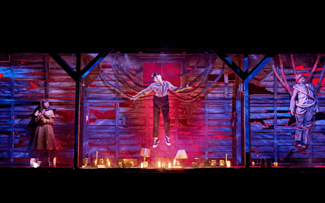 Performer suspended mid-air above candles on a dark immersive theatre stage in London