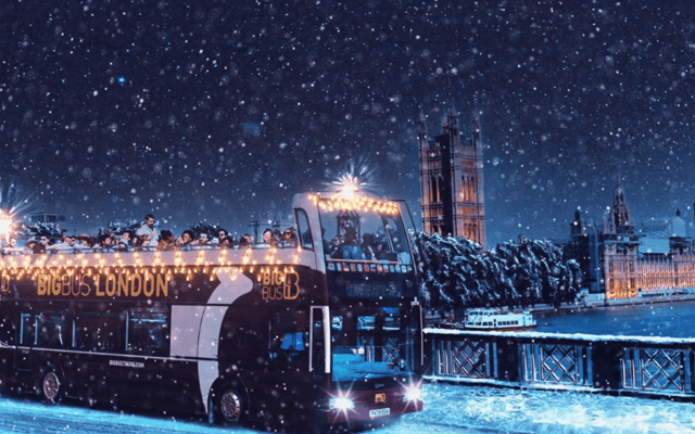 Big Bus London open-top tour bus lit up in the snow at night by Big Ben and Parliament