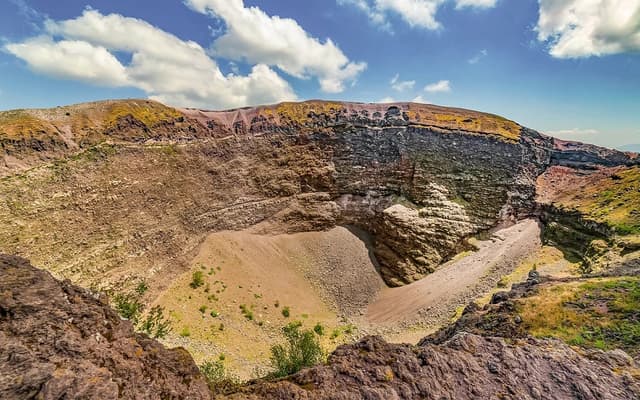 The wide rocky crater of Mount Vesuvius near Pompeii under a bright blue sky