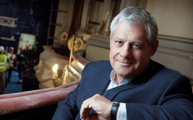 Theatre producer Cameron Mackintosh seated inside a London theatre with crew working behind him