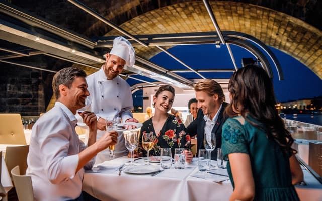 Chef serving guests at an elegant dinner table on a Prague river cruise boat at night