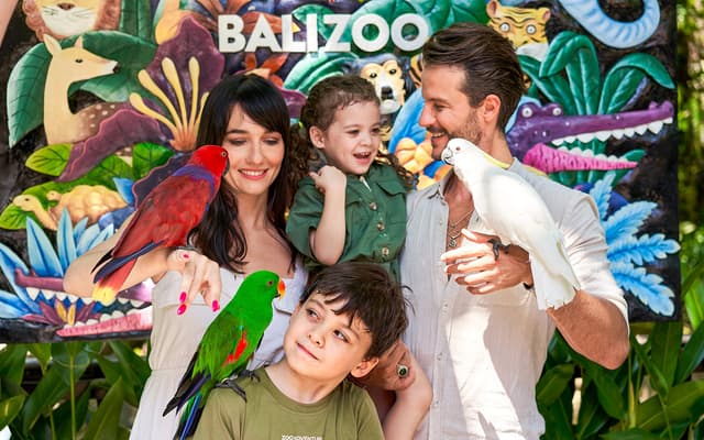 Family holding colourful parrots and a cockatoo in front of a Bali Zoo mural