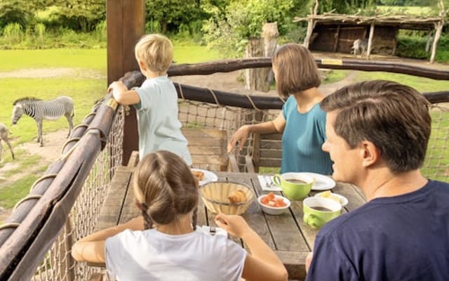 Family with a young child on a wooden platform watching animals at a green Leipzig zoo enclosure