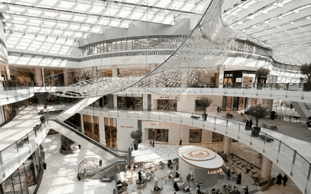 Sunlit luxury mall atrium in Dubai with a glass roof, multiple levels and designer storefronts