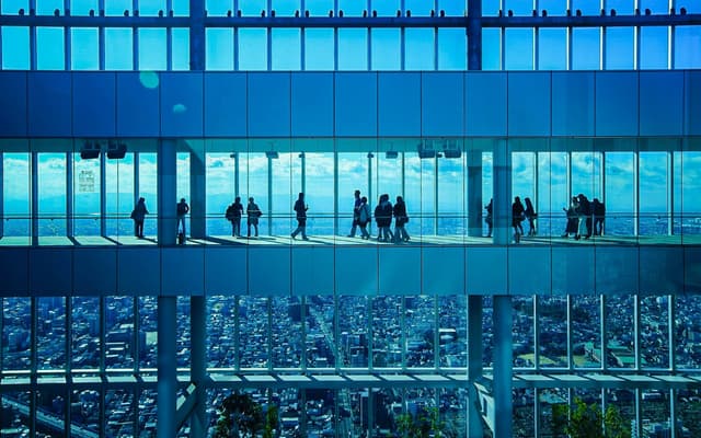 Visitors silhouetted on a high observation deck gallery overlooking the Osaka cityscape