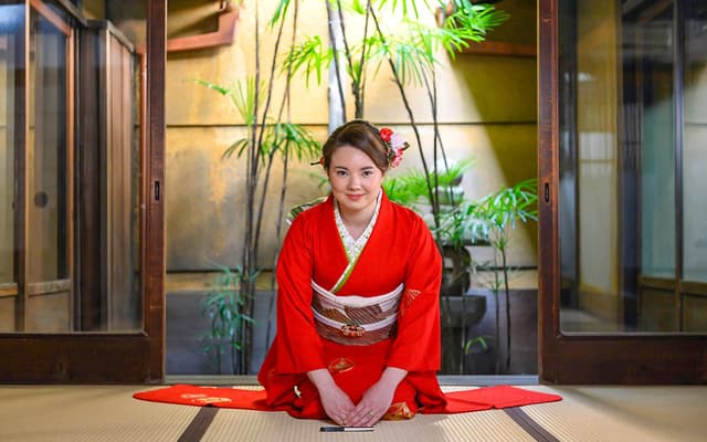 Woman in a red kimono kneeling on a tatami mat in a traditional Kyoto tea room