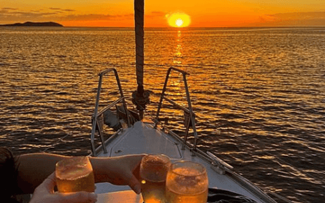 Friends toasting with sparkling drinks on a boat bow at sunset over the sea off Ibiza