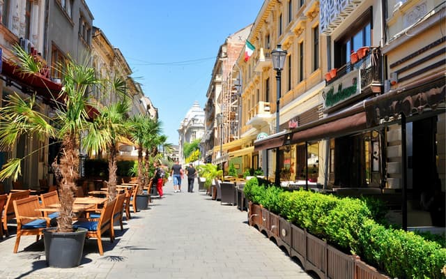 Sunlit cafe terraces and historic facades along an Old Town pedestrian street in Bucharest
