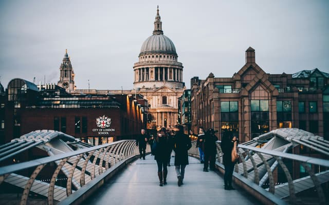 People crossing the Millennium Bridge towards St Paul's Cathedral at dusk in London