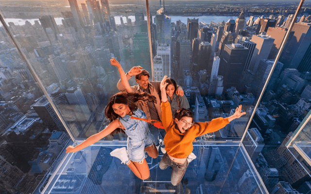 Family on the glass-floored observation deck at Summit One Vanderbilt above the New York skyline at sunset