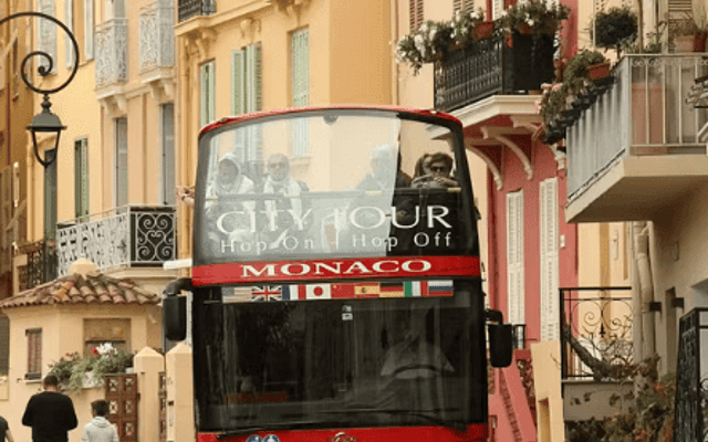 Red open-top City Tour sightseeing bus on a narrow pastel street in Monaco