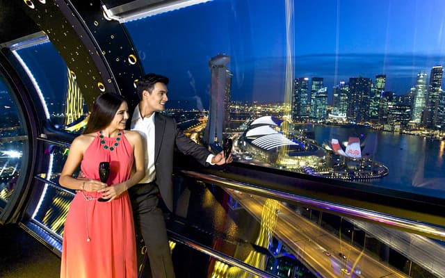 Couple with champagne in a Singapore Flyer capsule overlooking the Marina Bay skyline at night