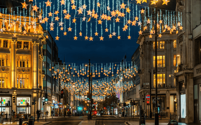 Star-shaped Christmas lights strung across Oxford Street in London at dusk with shops lit up