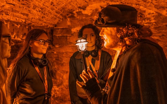 Costumed guide with a lantern leading a tour group through Edinburgh's underground stone vaults