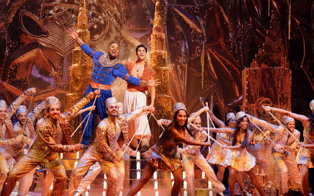 Disney's Aladdin musical on Broadway, the Genie and Aladdin centre stage with the gold-costumed ensemble