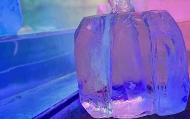 Ice-carved pumpkin sculpture glowing under colourful lights in a Cologne IceBar at Christmas