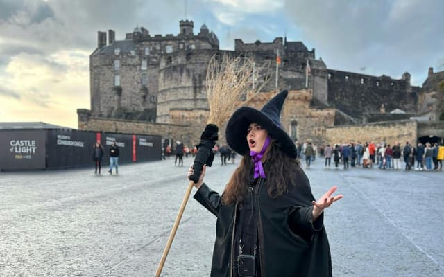 A costumed witch guide with a broomstick in front of Edinburgh Castle
