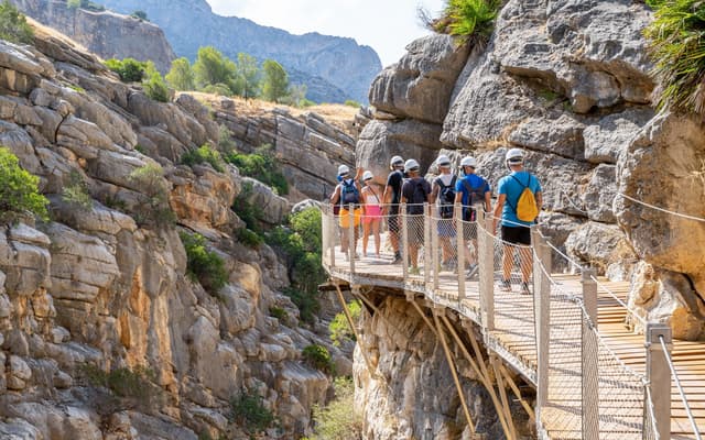 A guided group in helmets walking the wooden Caminito del Rey boardwalk fixed to the canyon wall