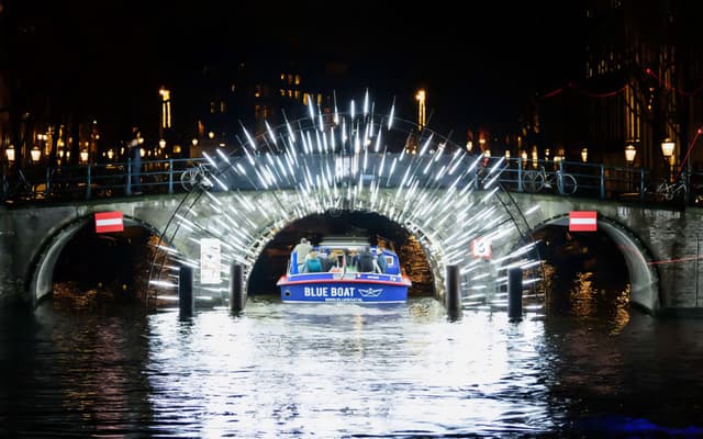 A canal boat passing under a glowing light artwork during the Amsterdam Light Festival
