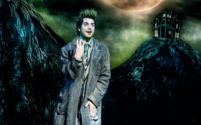 The green-haired title character of Beetlejuice the Musical under a haunted moonlit sky