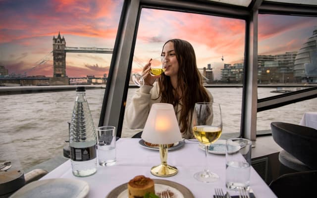Couple dining on a Thames sunset cruise with Tower Bridge behind