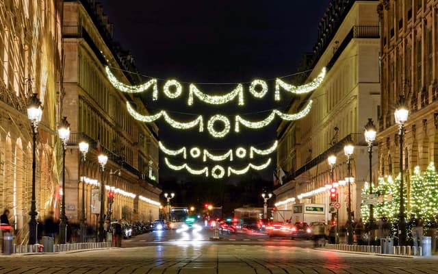 Christmas light garlands strung across a Paris street at night, lined with lit-up buildings