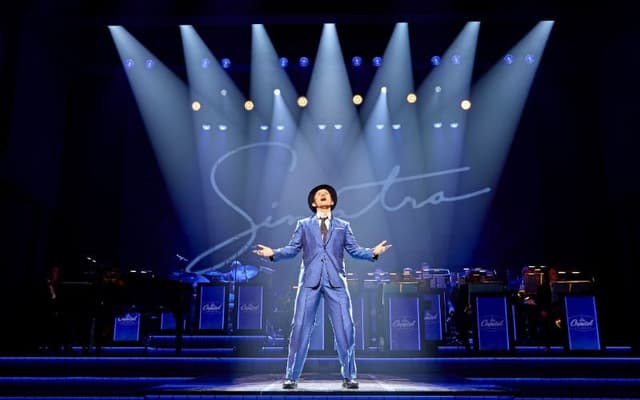 Joel Harper-Jackson as Frank Sinatra under blue spotlights in Sinatra: The Musical at the Aldwych Theatre