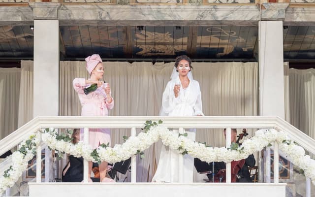 Two performers raise a toast on the balcony of the Globe stage in Much Ado About Nothing