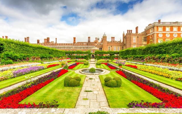 The formal gardens and Tudor brick facade of Hampton Court Palace on a summer day
