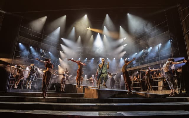 The company of Jesus Christ Superstar on stage under rows of spotlights