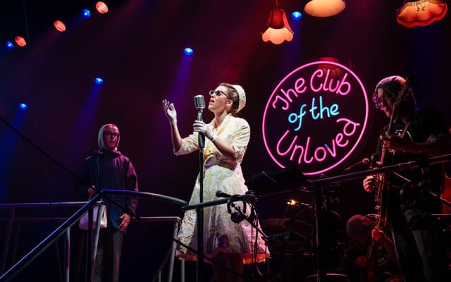 The Club of the Unloved performing under a neon sign in Tristan and Yseult