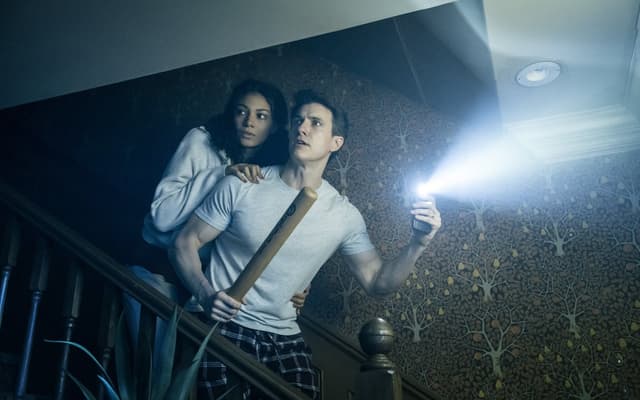 A couple on the staircase with a torch beam cutting through the dark in the London production of Paranormal Activity. Photo by Johan Persson