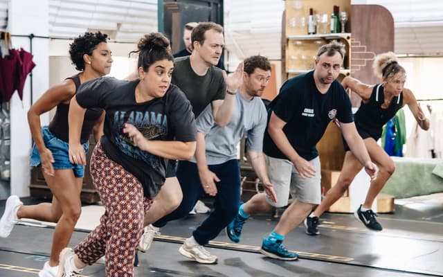 The company of The Comedy About Spies mid-scene in rehearsal, running across the studio floor
