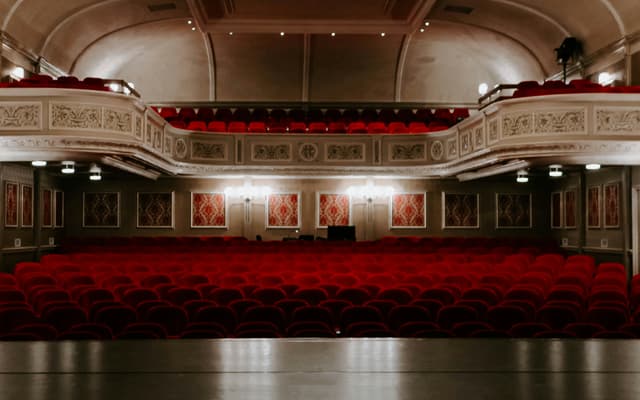 The interior of a grand West End theatre with red seats across the stalls and circle levels