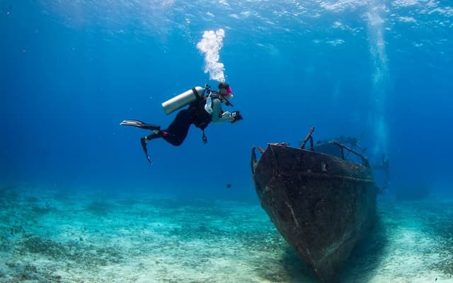Scuba diver exploring a sunken shipwreck on the seabed in clear blue water near Brisbane
