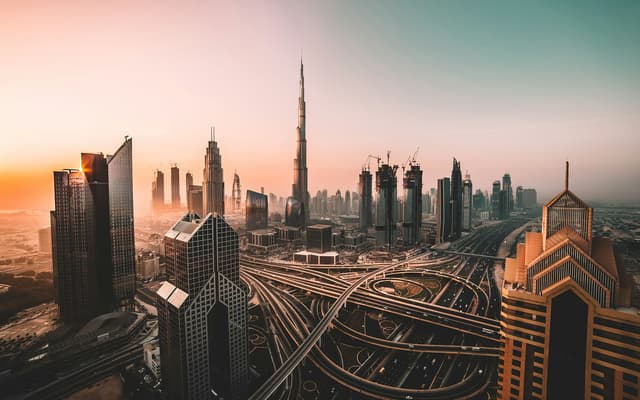 Dubai skyline at sunset with the Burj Khalifa rising above downtown towers and a highway interchange
