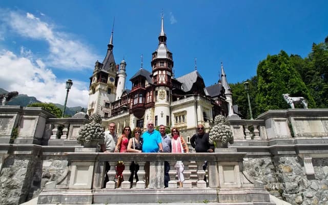 Fairytale Peles Castle near Bucharest, Romania, with visitors posing on the stone steps in summer