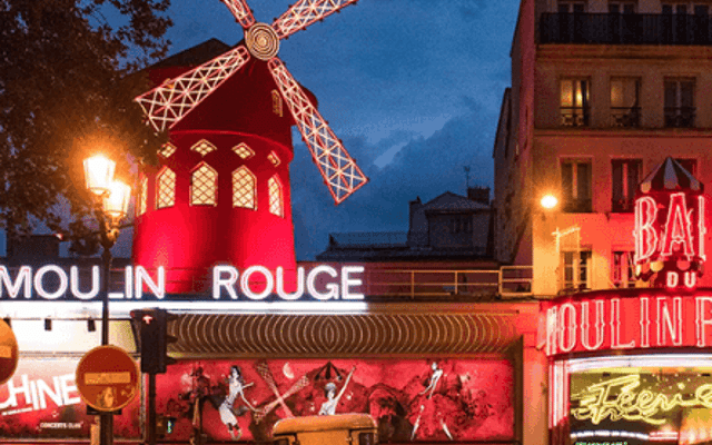 The Moulin Rouge red windmill cabaret lit up at dusk in Montmartre, Paris